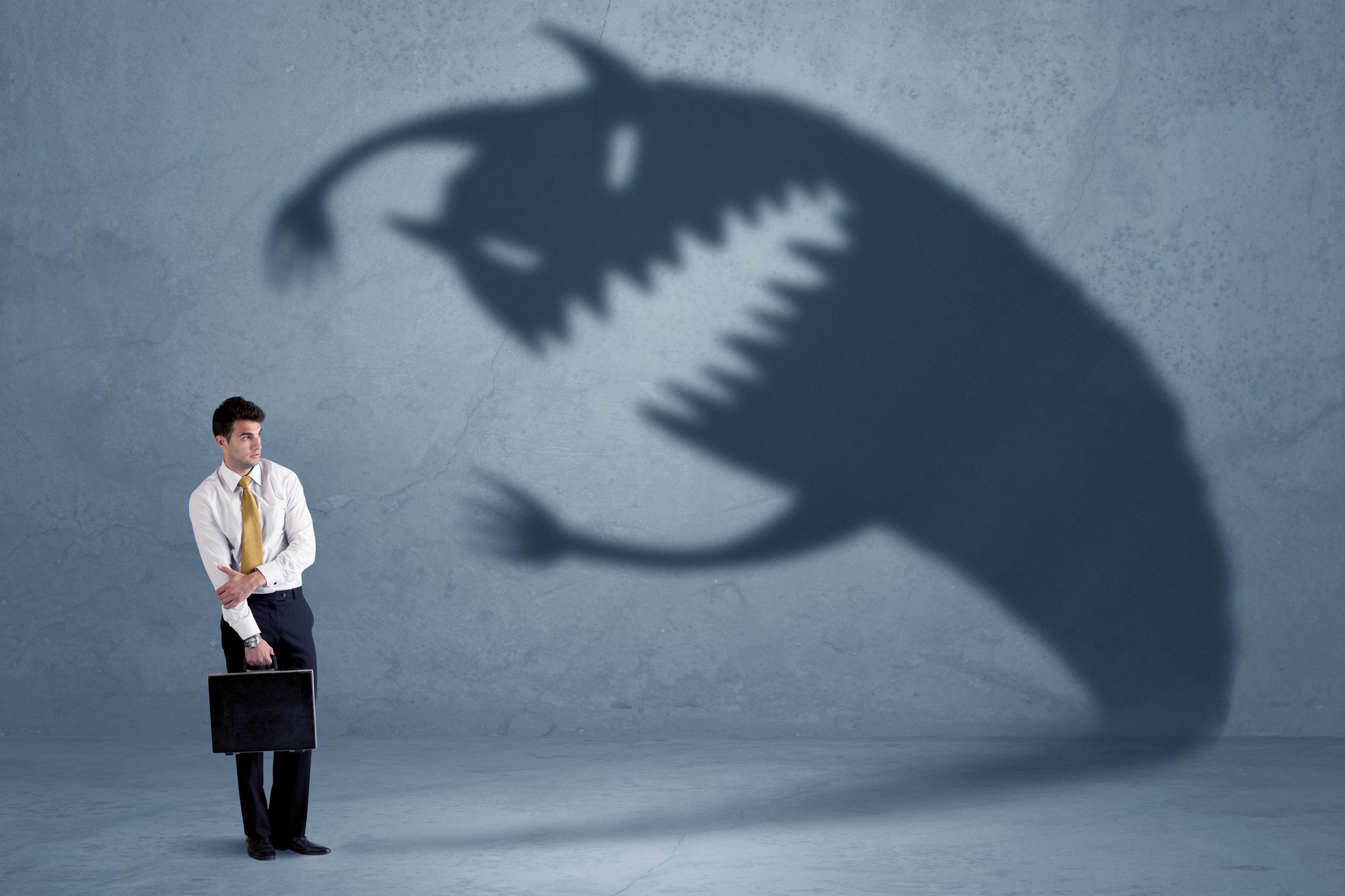 Businessman man with brief case afraid of monster seen in shadow against wall
